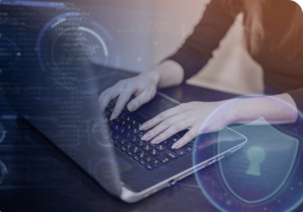 Mani che digitano su una tastiera di laptop con sovrapposizione di codice informatico e icona di scudo digitale, simbolo di cybersecurity