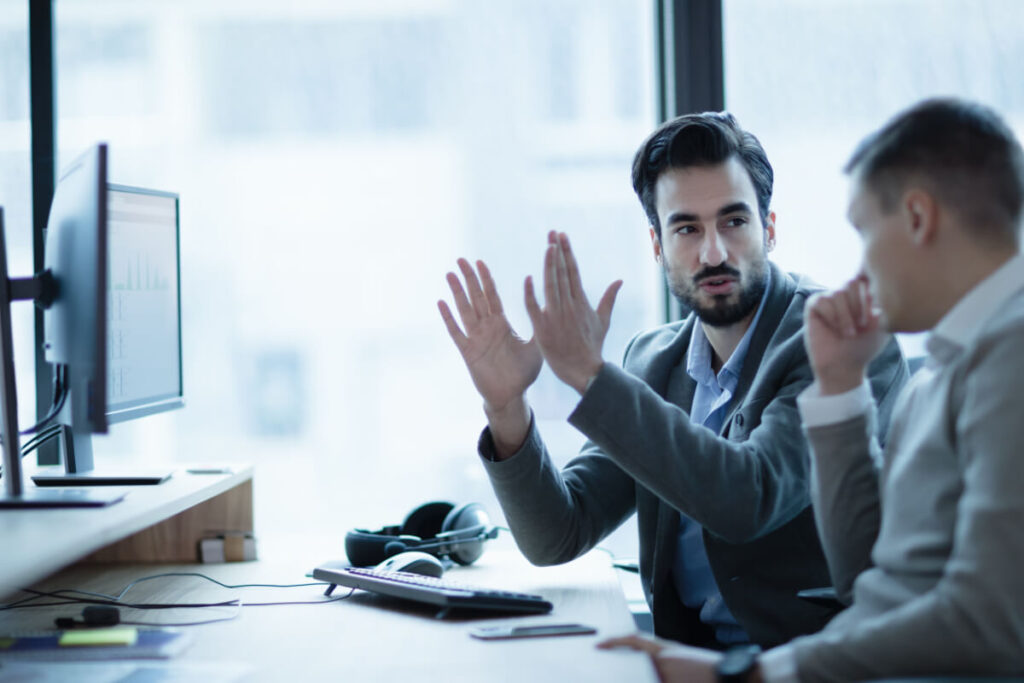 Due professionisti in abiti formali discutono davanti a un monitor con grafici in un ufficio moderno