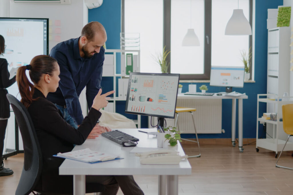 Due colleghi esaminano insieme grafici e dati su un monitor in un ufficio moderno, con una lavagna sullo sfondo