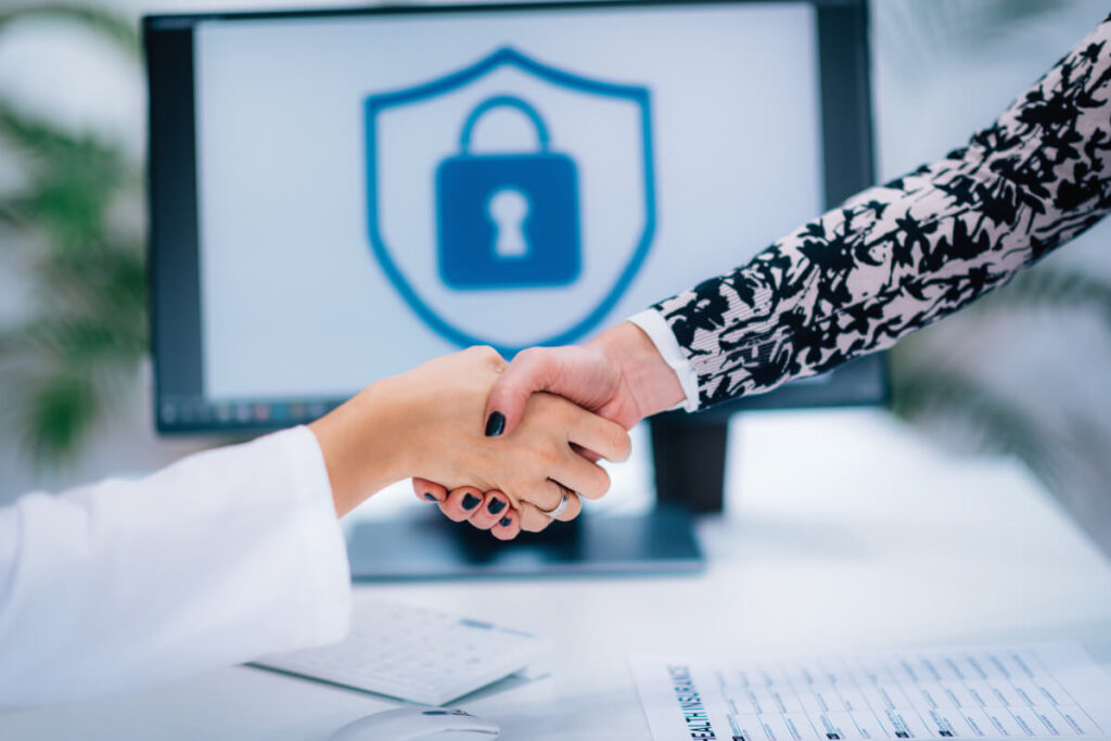 Stretta di mano tra due persone in un contesto professionale, con uno schermo sullo sfondo che mostra un'icona di sicurezza a forma di scudo con lucchetto