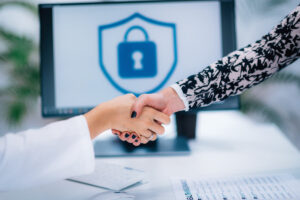 Stretta di mano tra due persone in un contesto professionale, con uno schermo sullo sfondo che mostra un'icona di sicurezza a forma di scudo con lucchetto