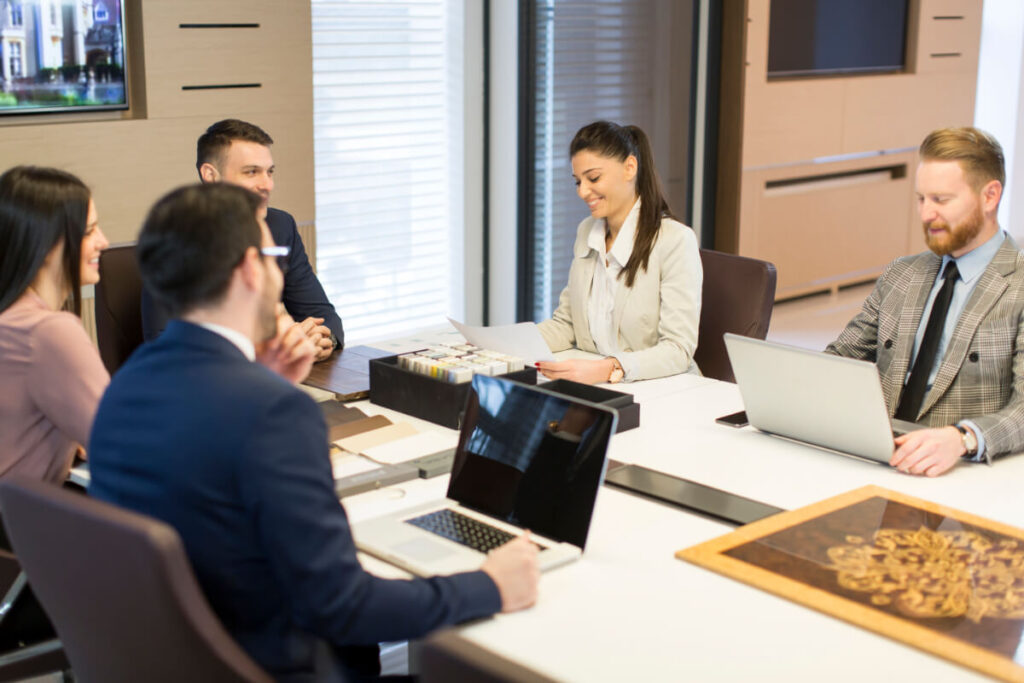Cinque professionisti riuniti attorno a un tavolo conferenze con laptop aperti durante una riunione in una sala meeting elegante