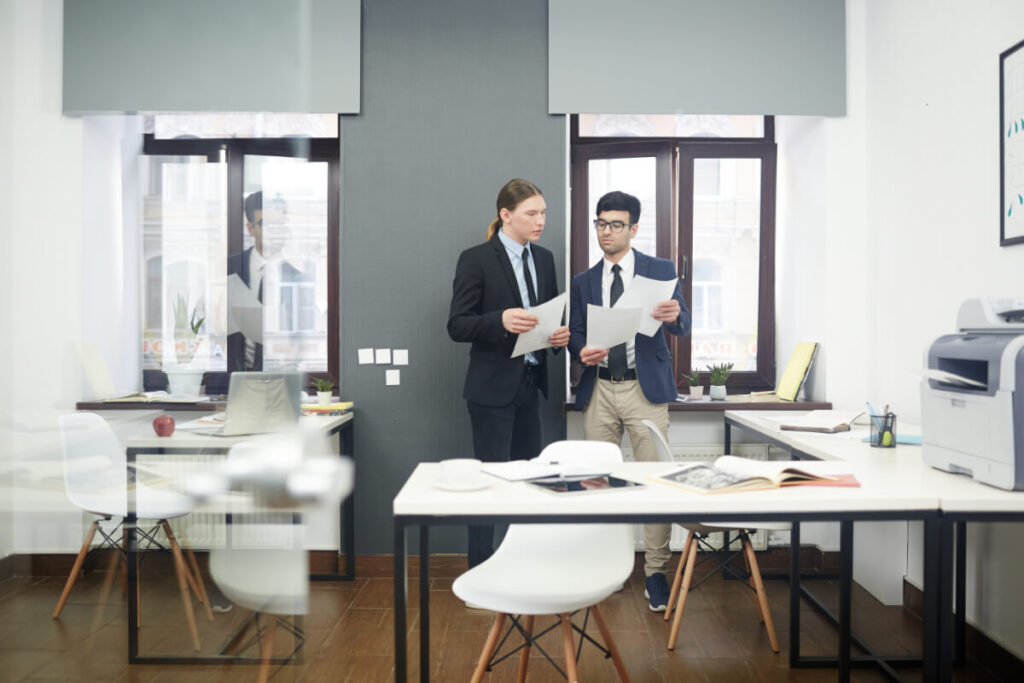 Due professionisti in abiti formali esaminano documenti in piedi all'interno di un ufficio moderno